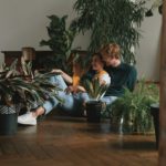 Beautiful young couple watering houseplants while sitting on the floor at home