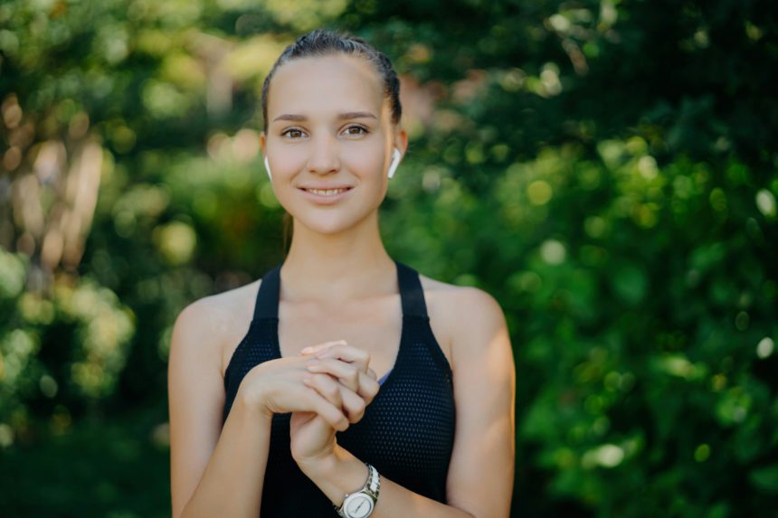 Fit, young woman with earphones, smiling in a lush park, post-workout