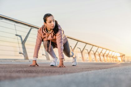 Sporty girl is preparing for jogging on the bridge with sunlight behind