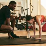 Strong sportswoman exercising with instructor at gym