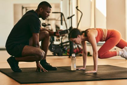 Strong sportswoman exercising with instructor at gym