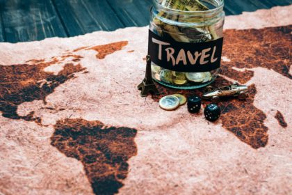 Travel budget concept. Money saved for vacation in glass jar on world map background, copy space.